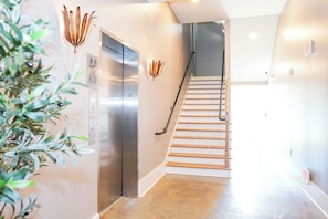 A modern interior with a staircase, a wall-mounted light fixture, and an elevator.