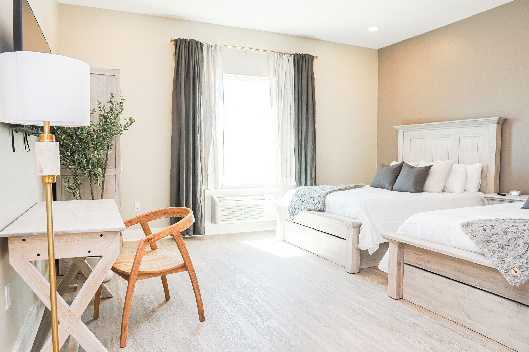 Una habitación de hotel con cama, mesita de noche, lámpara, sillón y ventana con cortinas.
