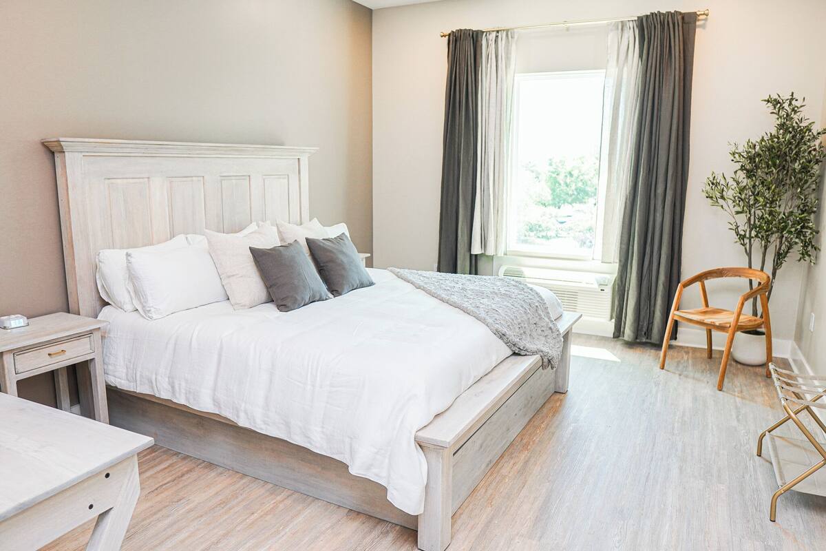 Une chambre à coucher avec un lit, des tables de chevet, une chaise et une fenêtre avec des rideaux.