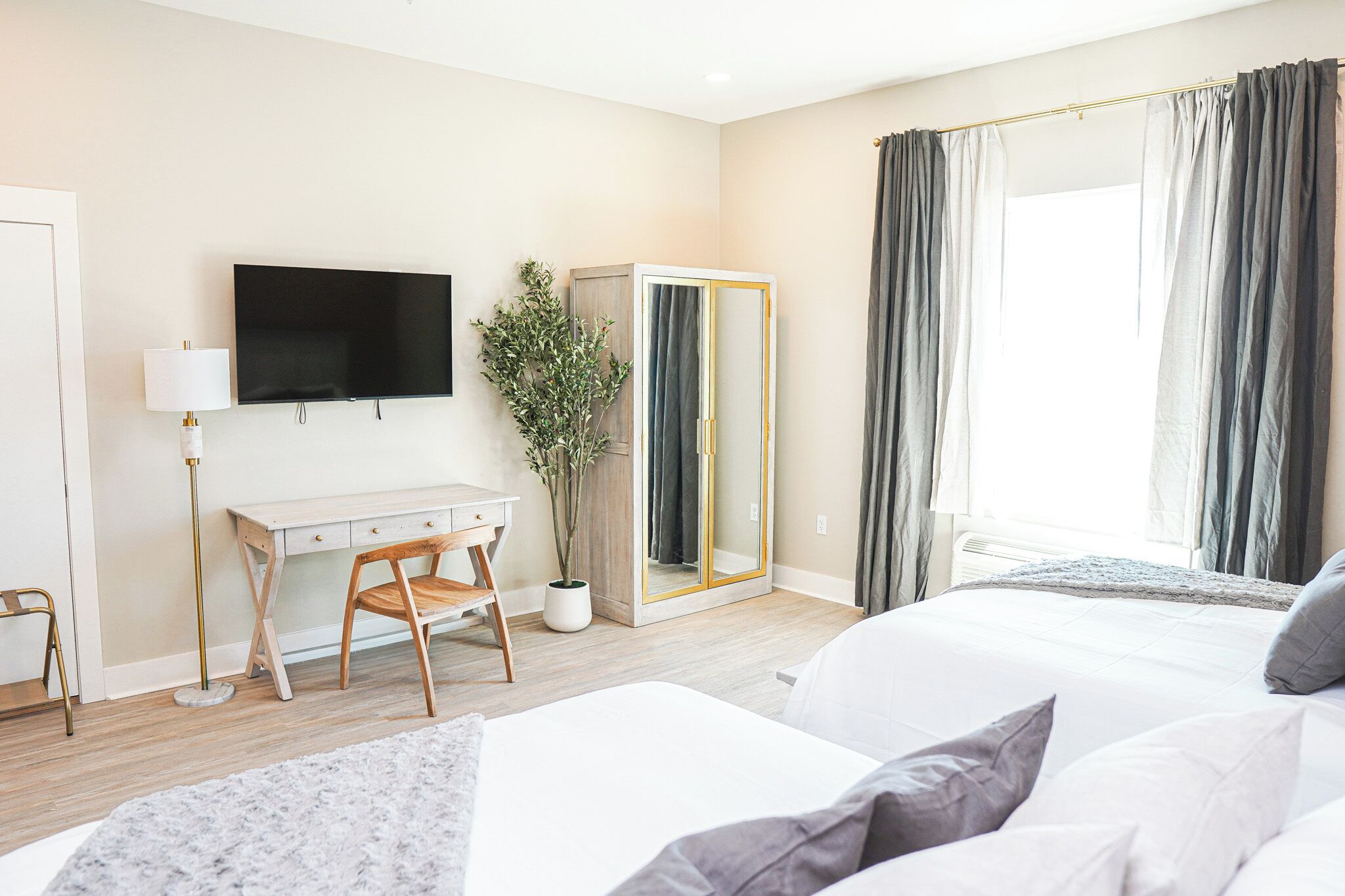 A hotel room with a bed, a desk with a chair, a TV, a wardrobe, and a large window with curtains.