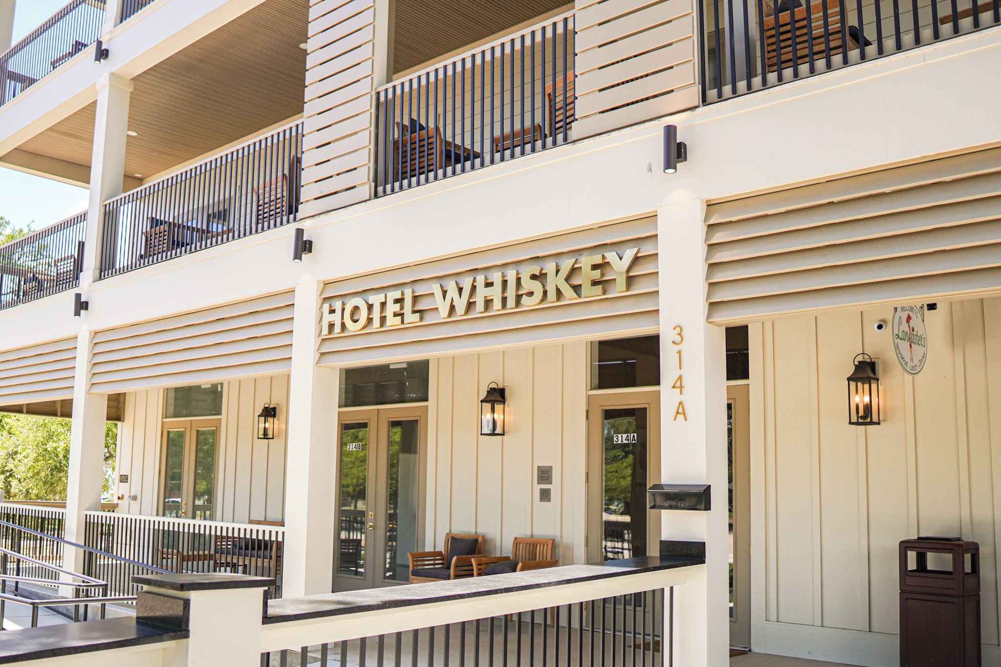 Un hotel con un letrero 'HOTEL WHISKEY', un balcón con barandilla de madera y una entrada principal con una puerta marcada '314A'.