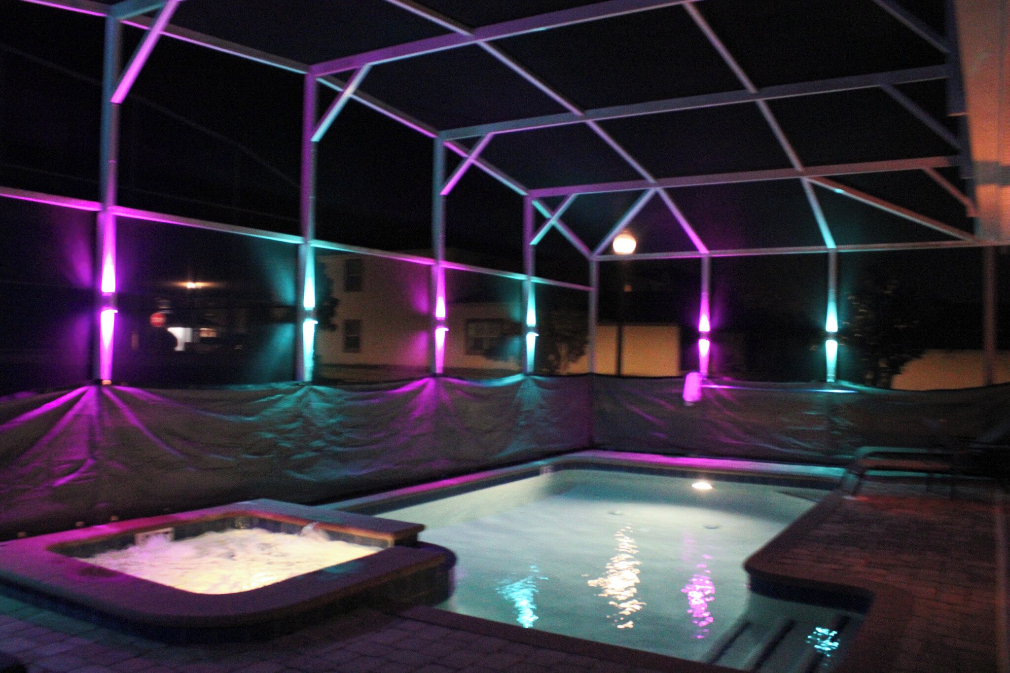 A pool area with a geometric structure overhead, a hot tub, and a small seating area.