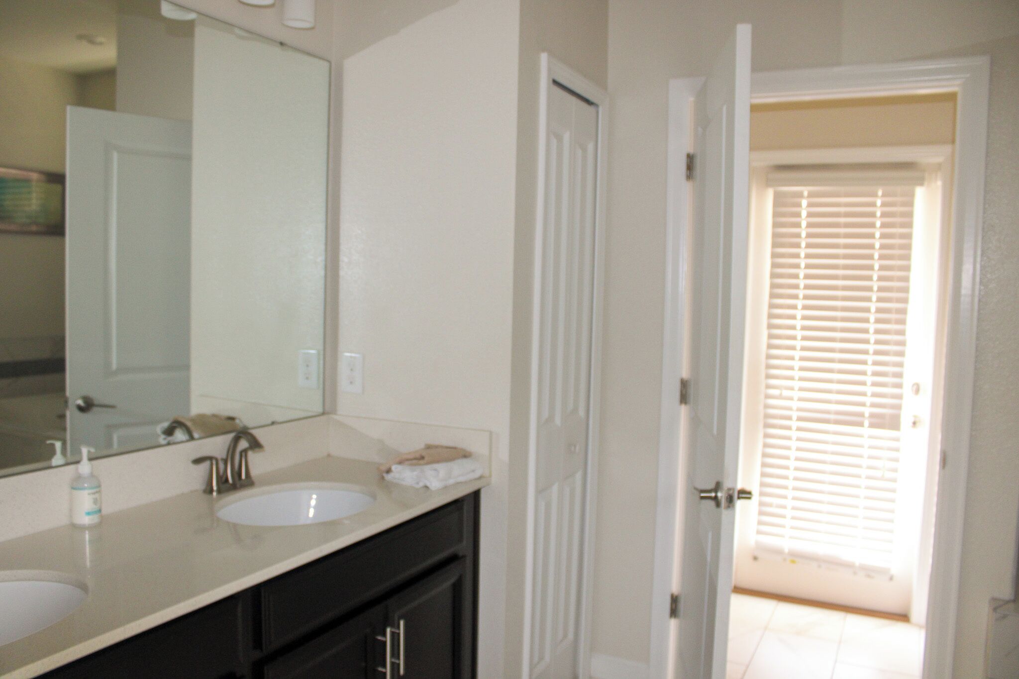 A bathroom with a double sink, a large mirror, and a door leading to another room.