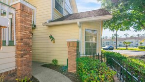 A residential building with a brick column, a small porch, and a green fence. - 3BR family condo | steps from Laguna Bay pool (Kissimmee)
