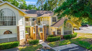 A two-story house with a front porch, a small attached garage, and a visible driveway. - 3BR family condo | steps from Laguna Bay pool (Kissimmee)