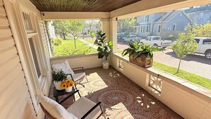 Une véranda abritée avec une chaise, une petite table ornée d’un vase de tournesols et des plantes en pot.