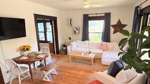 Un salon comprenant un canapé, une table basse, une table à manger avec des chaises, un téléviseur fixé au mur et un ventilateur de plafond.