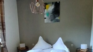 A bedroom with a wooden bed, white bedding, a hanging light fixture, a painting on the wall, and a bedside table with a lamp. - In the heart of nature - Gîtes 15 people (Windstein)