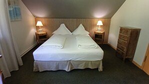 A neatly made bed with pillows and towels, two bedside lamps, a wooden dresser, and a sloped ceiling. - In the heart of nature - Gîtes 15 people (Windstein)