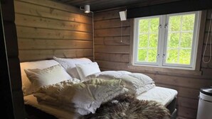 Una habitación de cabaña de madera con cama, ventana y cubo de basura.