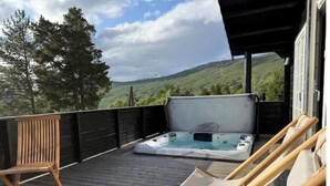 Una terraza de madera con un jacuzzi, sillas de descanso y vistas a un paisaje verde.