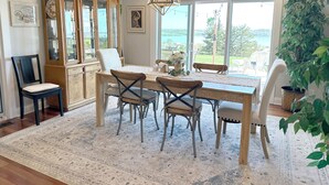 Un comedor con una mesa de madera, sillas, una araña y ventanas grandes con vistas al exterior.