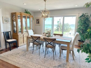Un comedor con una mesa de madera, sillas, una araña y ventanas grandes con vistas al exterior.