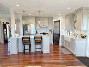 A kitchen with white cabinetry, a central island with two chairs, a stainless steel refrigerator, and a gas stove.