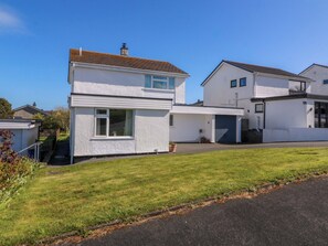 A two-story residential building with a garage, a small garden, and a clear sky. - 20 Gwelfor Estate (Cemaes Bay)