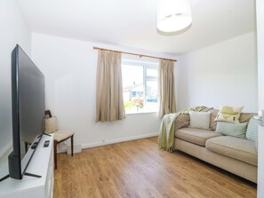 A living room with a flat-screen TV, a sofa, a window with curtains, and a wooden floor. - 20 Gwelfor Estate (Cemaes Bay)