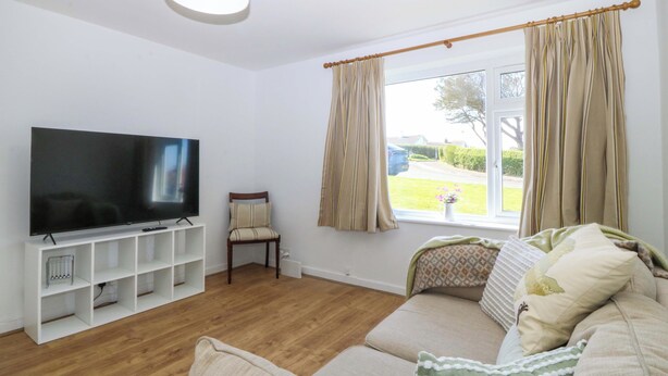 Uma sala de estar com televisão, sofá e janela com cortinas.