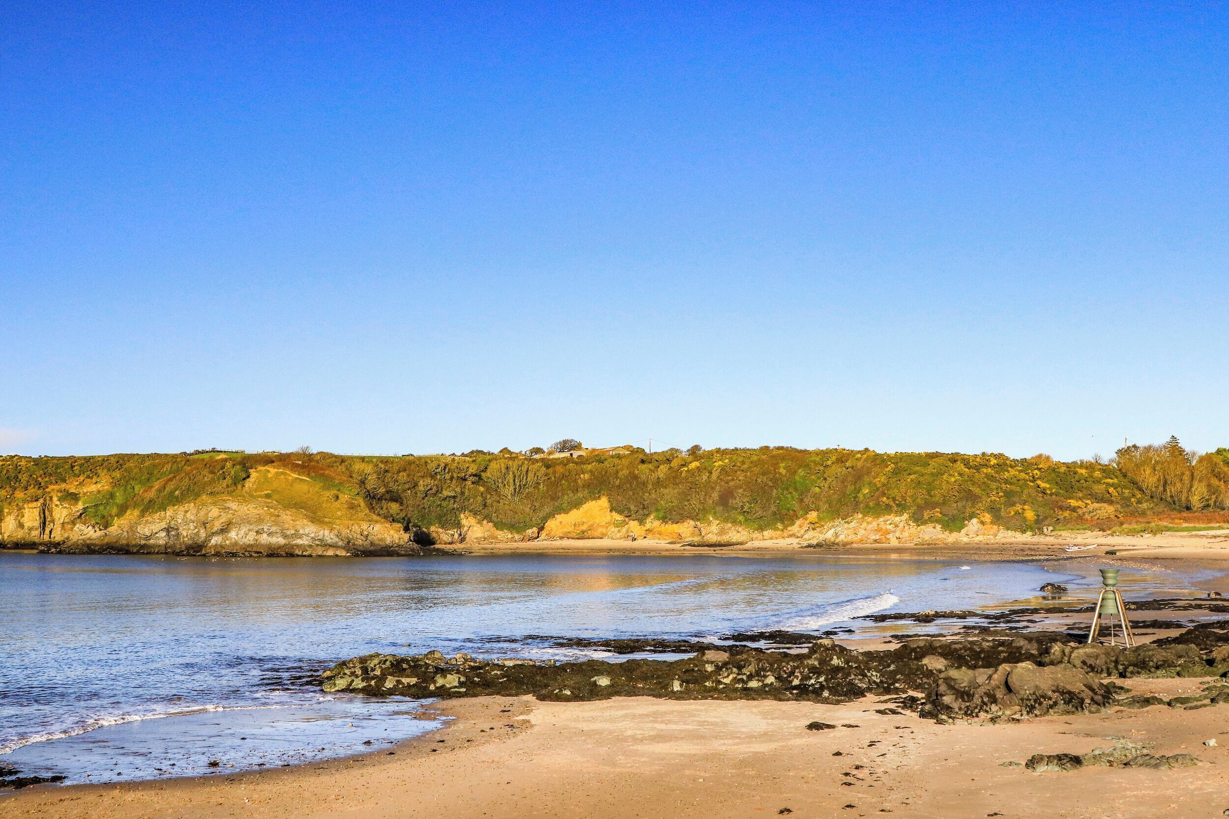 Ein Strand mit klarem Himmel, sandigem Ufer und Felsenformationen.