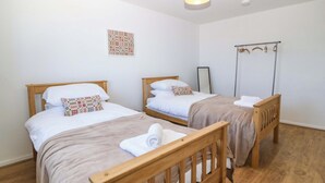Quarto com duas camas de madeira, roupa de cama branca, luminária pendente e um quadro na parede.