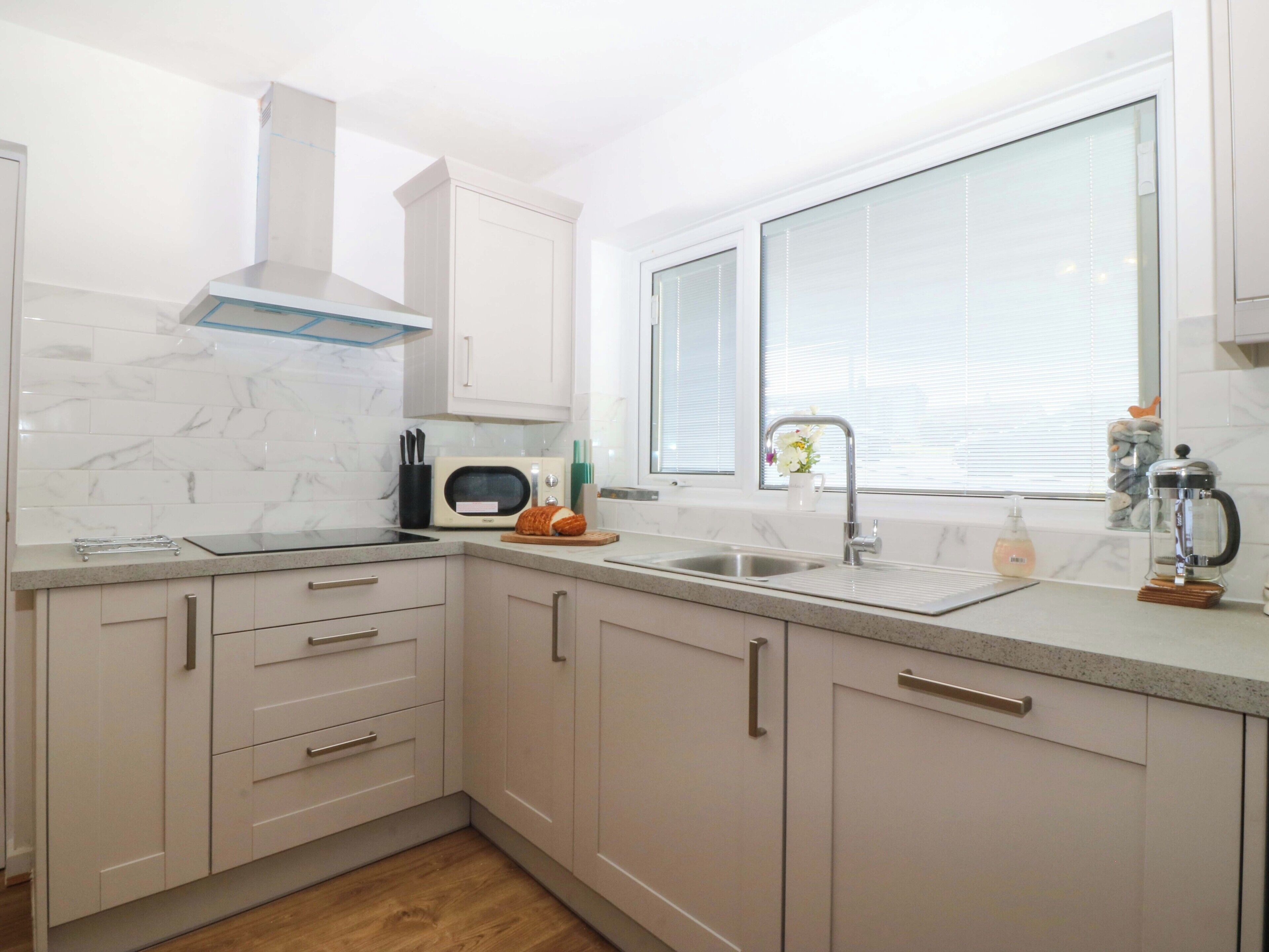A modern kitchen with white cabinets, a built-in microwave, a stainless steel sink, and a window with blinds.
