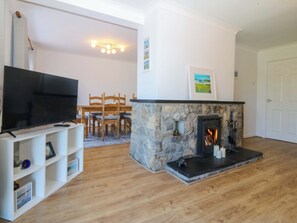 A living room with a fireplace, a television, a dining area with chairs, and a white door. - 20 Gwelfor Estate (Cemaes Bay)