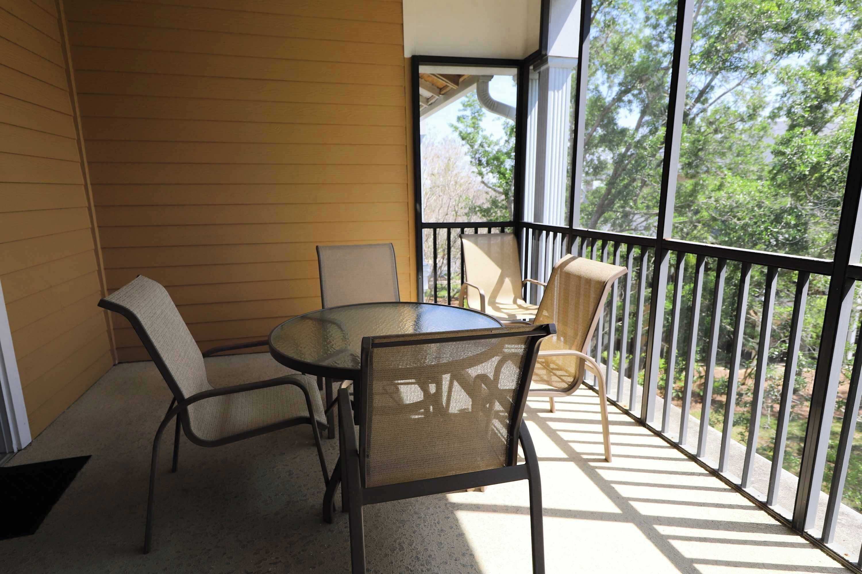 A balcony with a table and chairs, a view of trees, and a railing.