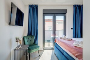 A hotel room with a bed, a green armchair, a small table with decorative items, and a TV mounted on the wall. - Panorama Coastal Haven (Split)
