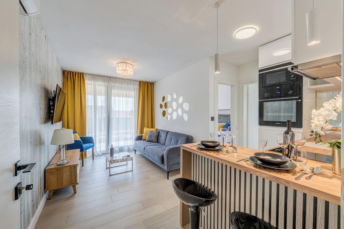 A modern kitchen with a built-in oven and microwave, a dining area with a bar, and a living room with a sofa and coffee table.