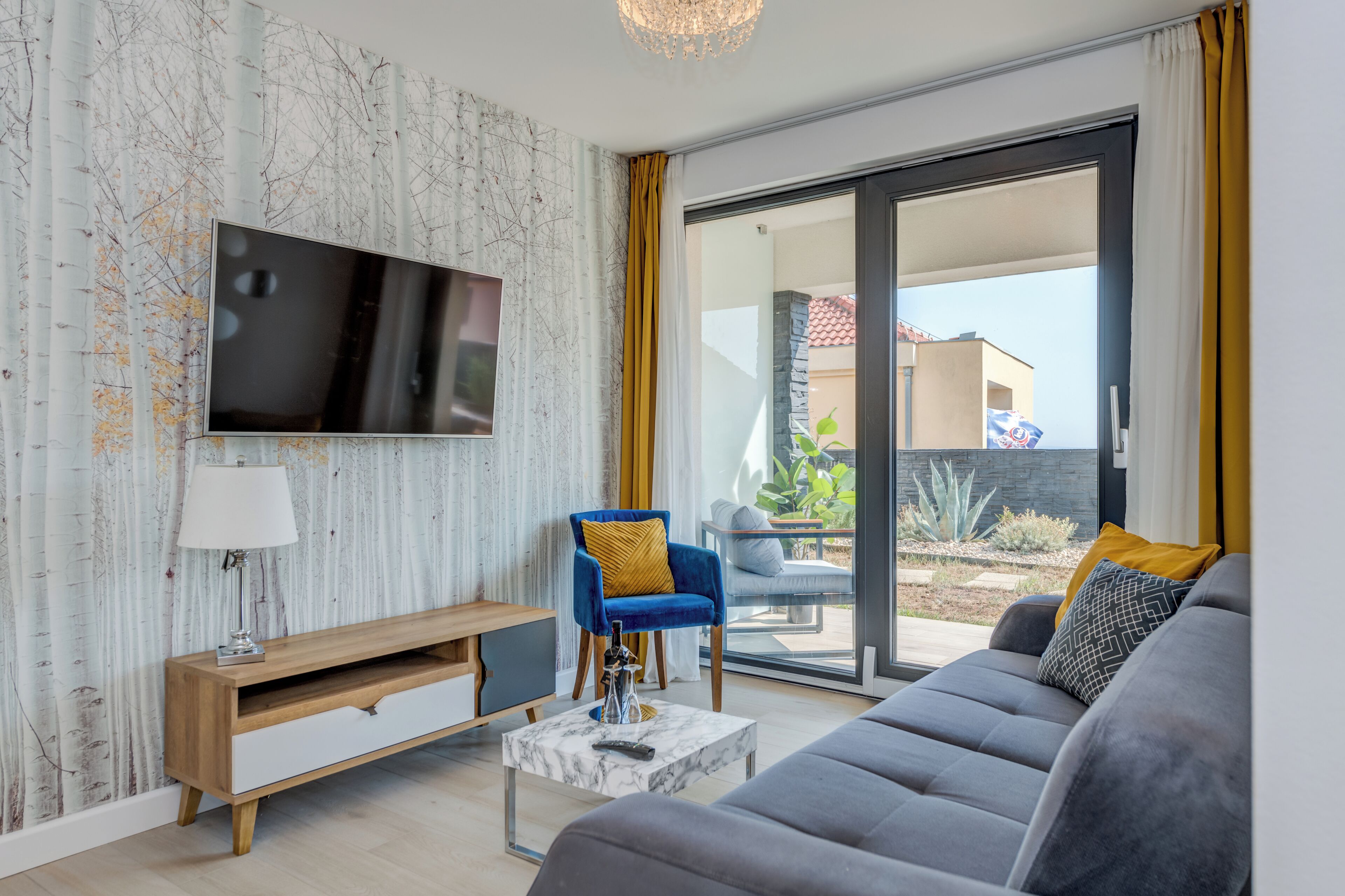 Ein modernes Wohnzimmer mit Flachbildfernseher, einer Couch, einem blauen Sessel und einem Marmortisch.