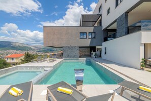 Un edificio moderno con piscina, sillas de descanso y vistas a las montañas.