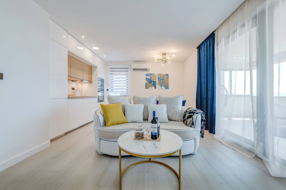 A modern living room with a sofa, a coffee table, and a kitchen area in the background.
