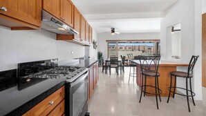 Una cocina moderna con armarios de madera, estufa a gas y una zona de comedor con taburetes de bar.
