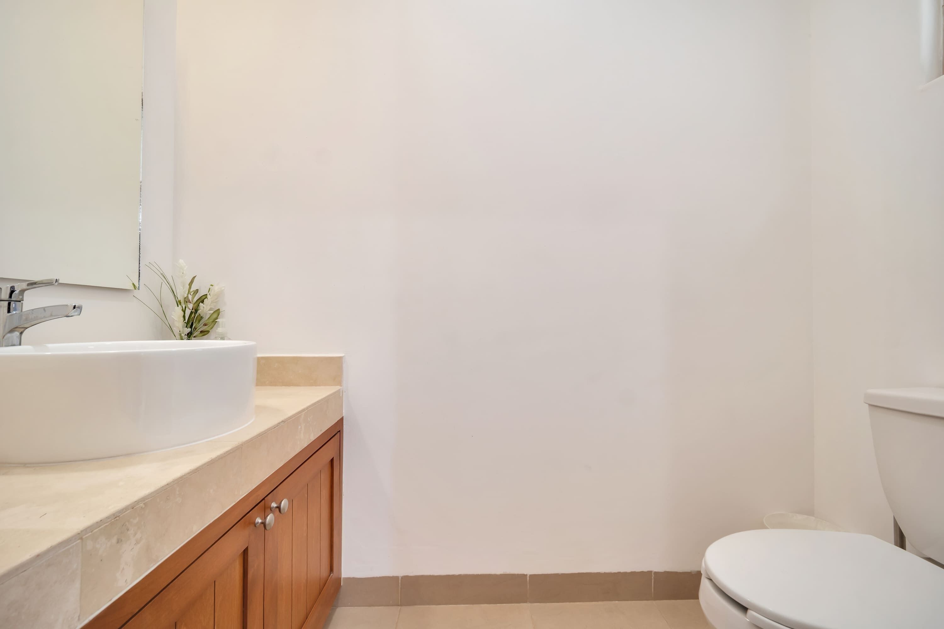 Un baño con lavamanos blanco, armarios de madera, un espejo y un inodoro.