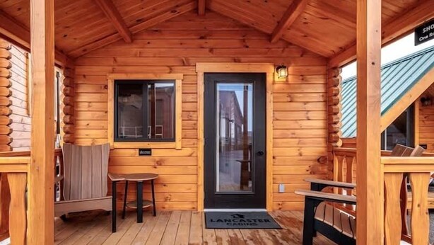 A wooden cabin with a front door, a bench, a small table, and a window.