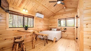 A wooden cabin interior with a bed, a dining table, and a ceiling fan.
