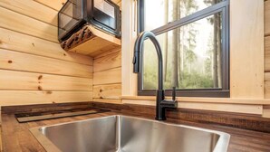 A modern kitchen with a stainless steel sink, a black faucet, and a window with a view of trees.