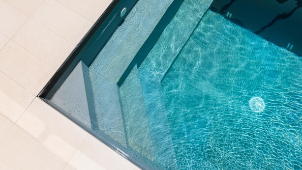 Ein klarer Blick auf ein Schwimmbecken mit Glasrand und Fliesenboden.