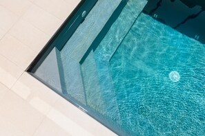 Vista nítida de uma piscina com borda de vidro e piso revestido de azulejos.