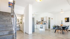 Eine moderne Küche mit weißen Schränken, ein Essbereich mit Tisch und Stühlen sowie eine Treppe mit Metallgeländern.
