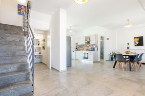 A modern kitchen with white cabinets, a dining area with a table and chairs, and a staircase with metal railings. - Villa Calaurisi - Noto (Noto)