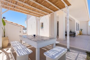 A covered outdoor seating area with a table and benches, a potted plant, and a view of the sky. - Villa Calaurisi - Noto (Noto)