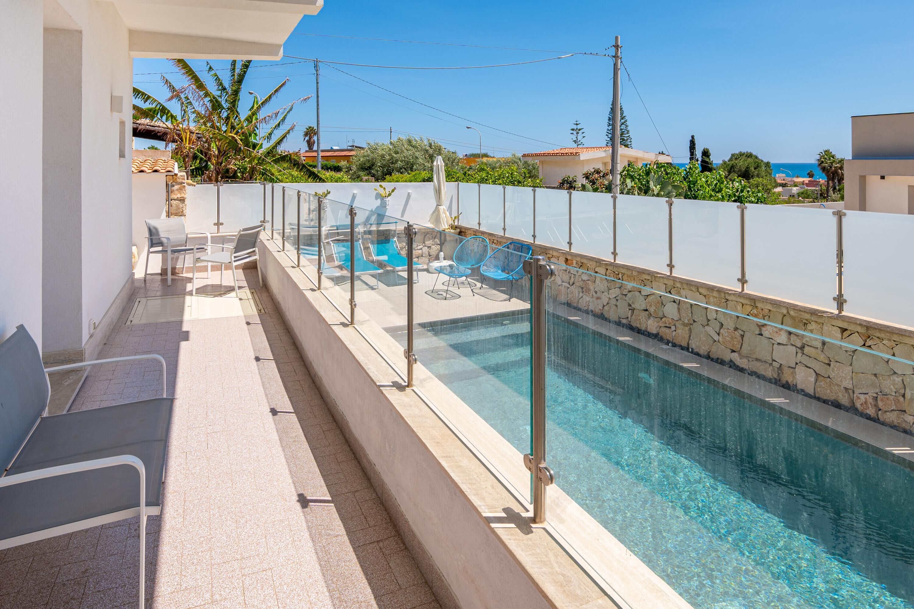 Ein Poolbereich mit freiem Blick auf das Meer, einer Steinmauer und einer überdachten Sitzgelegenheit.