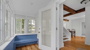 Ein Zimmer mit Holzboden, einer Bank, einer Tür zu einem anderen Raum und einer Treppe.
