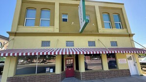 A yellow two-story building with a red and white striped awning, a sign for Upton's Apartments, and a brick foundation. - Historic King Suite in Upton's Confectionery (Globe)
