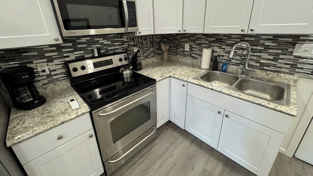 A kitchen with white cabinets, a stainless steel microwave, a stove, and a sink. - Historic King Suite in Upton's Confectionery (Globe)