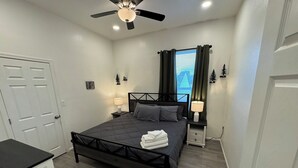 A bedroom with a bed, bedside tables, a ceiling fan, a window with curtains, and a door. - Historic King Suite in Upton's Confectionery (Globe)