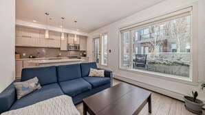 A modern apartment with a kitchen, a blue sofa, a coffee table, and large windows.