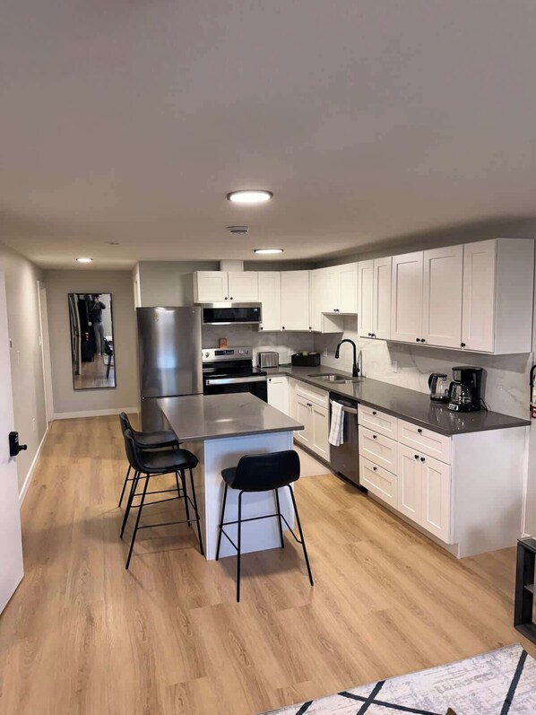 A modern kitchen with white cabinets, a stainless steel refrigerator, a microwave, and a coffee maker.