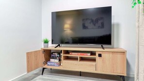 A flat-screen TV mounted on a wooden TV stand with a lamp and a plant beside it.
