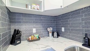 A modern kitchen with dark tiled walls, a marble countertop, a knife block, a toaster, and a sink. - Cozy 2 Bedroom Suite Near Ctrain Mall and Downtown (Calgary)